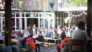 Un espace extérieur aménagé pour les repas, avec plusieurs tables et bancs en bois, entouré d’immeubles.