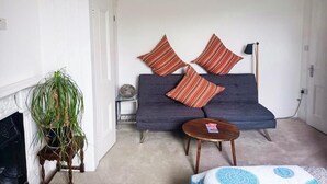 Un salon avec un canapé, des coussins à rayures, une petite table ronde et une plante en pot.