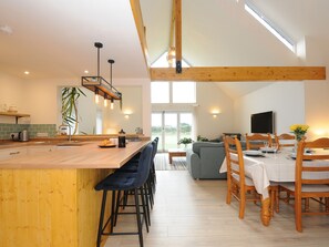 A modern kitchen with a wooden island, bar stools, and a dining area with a table set for two. - Gwennel Neyth (Newquay)