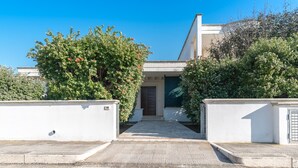 Una casa moderna amb entrada pavimentada, envoltada de verdura i un cel blau clar.