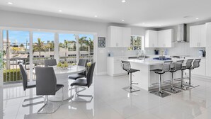 A modern kitchen with white cabinets, a central island with bar stools, and large windows offering a view of palm trees.