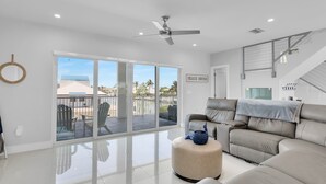 A spacious living room with a large sliding glass door leading to a balcony, a ceiling fan, and a staircase.