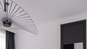 Ett modernt hotellrum med en platt-TV som är monterad på väggen, en matplats med ett runt bord och stolar, en soffa och en unik taklampa med svartvitt mönster.