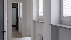 En hall med vita väggar, ett element och ett fönster med persienner.