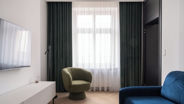 Un salon moderne avec un téléviseur à écran plat fixé au mur, un fauteuil vert, un canapé bleu et une table basse ronde.