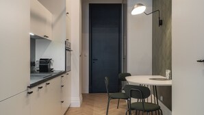 Une cuisine moderne avec des meubles blancs, une porte noire et un coin repas comprenant une table blanche et deux chaises.