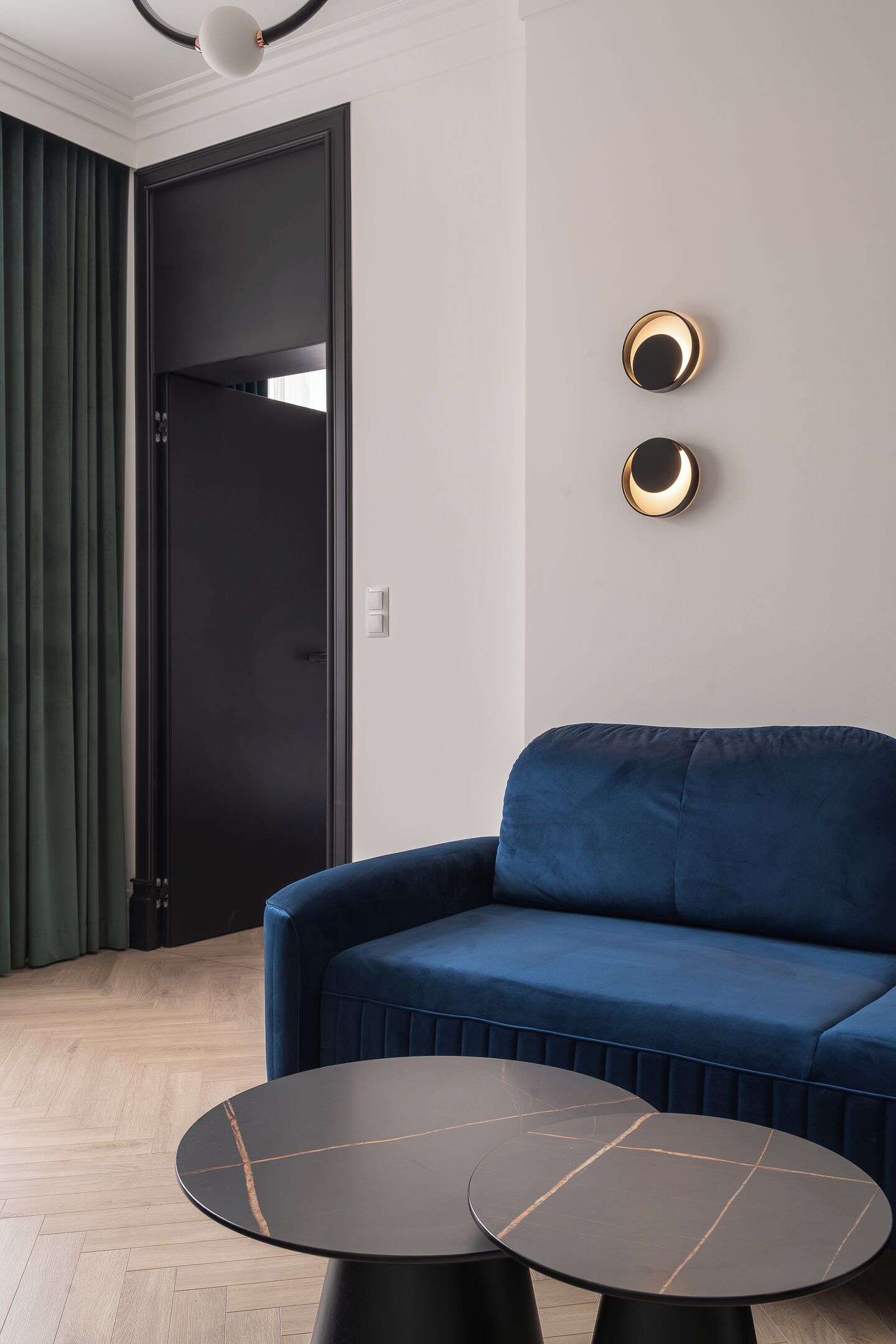 A modern living room with a blue sofa, two round black tables, and a black door.