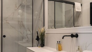 Une salle de bain moderne avec une douche à parois de verre, un meuble-lavabo blanc doté d'un grand miroir et des murs à motifs de marbre.
