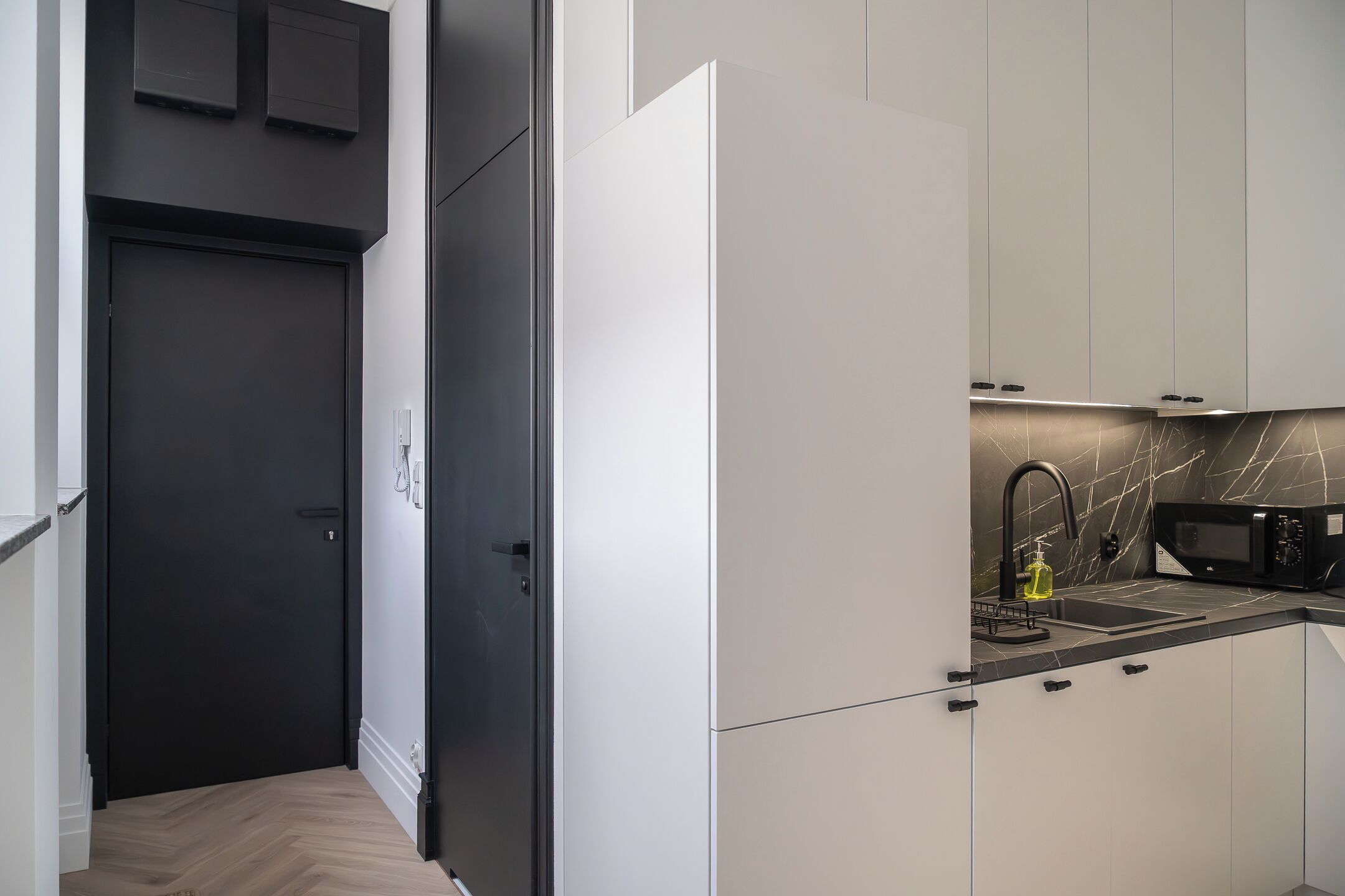 Una cocina moderna con armarios blancos, una puerta negra y un salpicadero de mármol.