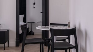 Ett modernt rum med ett runt bord och två stolar, ett litet sidobord och en säng med en svart sänggavel.