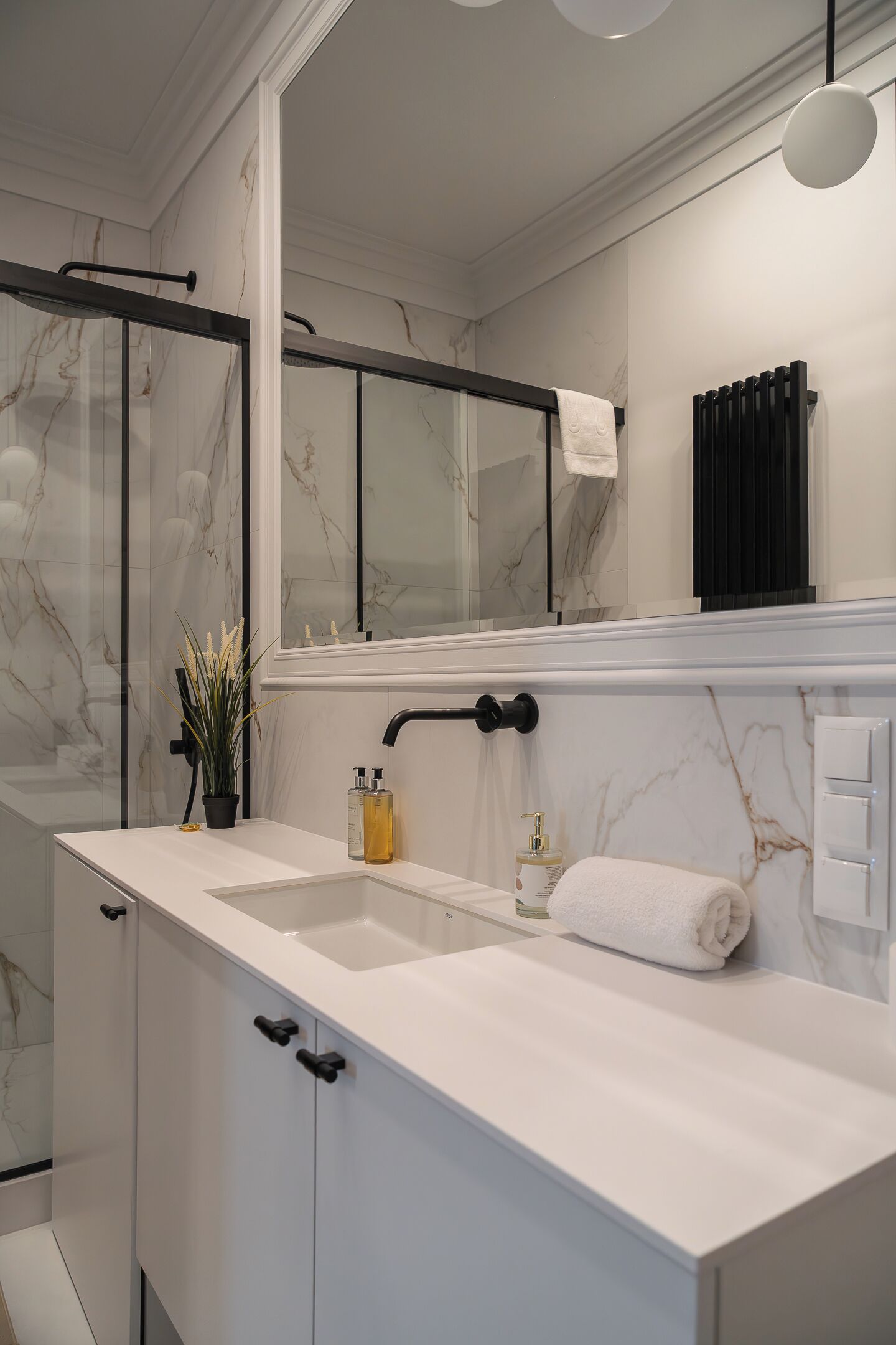 A modern bathroom with a marble backsplash, a large mirror, and a white countertop.