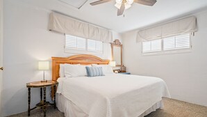 A bedroom with a wooden headboard, a bedside table with a lamp, and a ceiling fan. - Ground level bay-front home on deep waterfront!  (Dauphin Island)