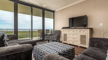 A spacious balcony with a large sliding glass door, a flat-screen TV mounted on a cabinet, and a patterned ottoman.