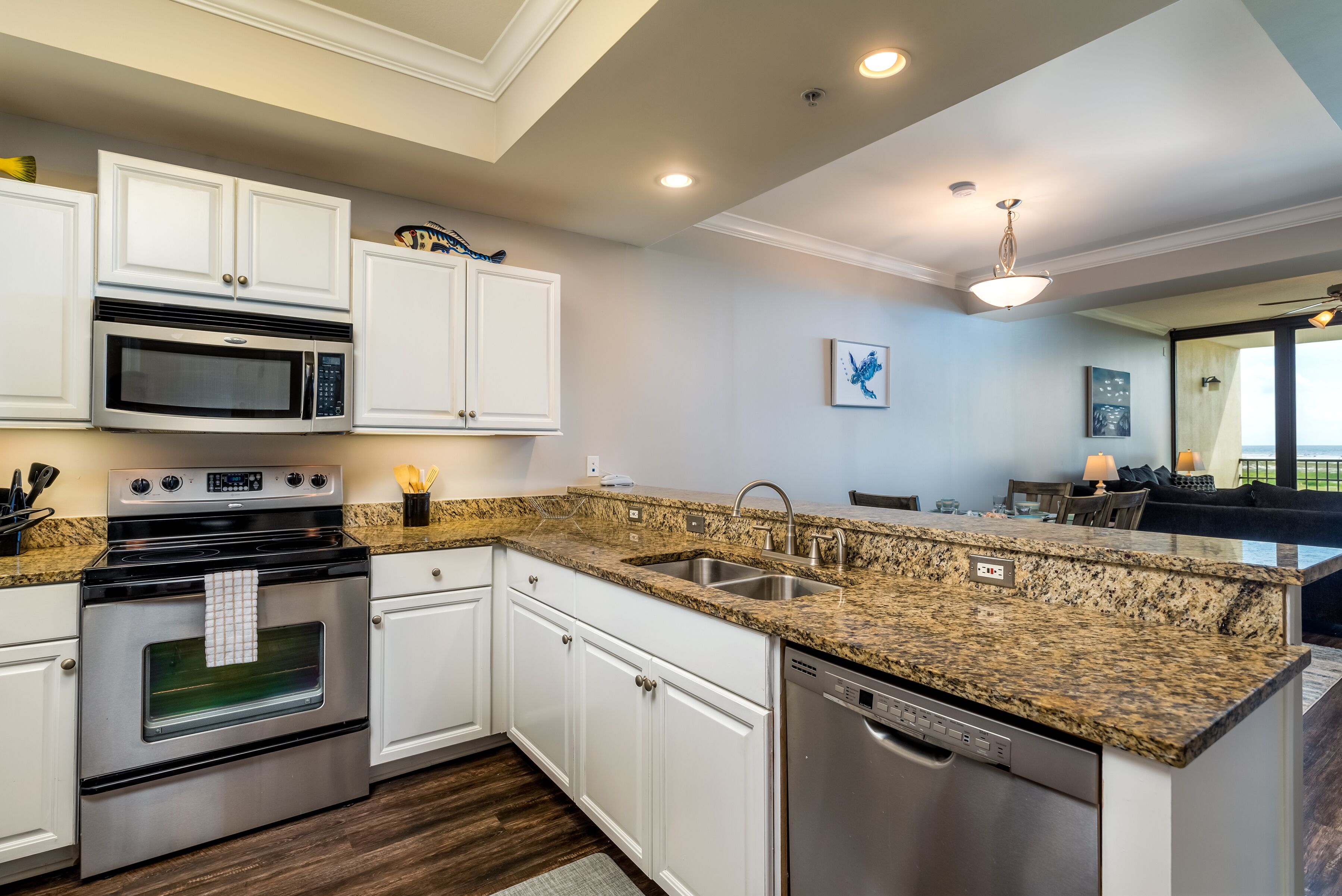 A modern kitchen with white cabinetry, granite countertops, stainless steel appliances, and a built-in dishwasher.
