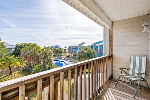 A wooden balcony with a view of a swimming pool and surrounding buildings. -   Beautiful Gulf View Home steps away from the beach! (Dauphin Island)