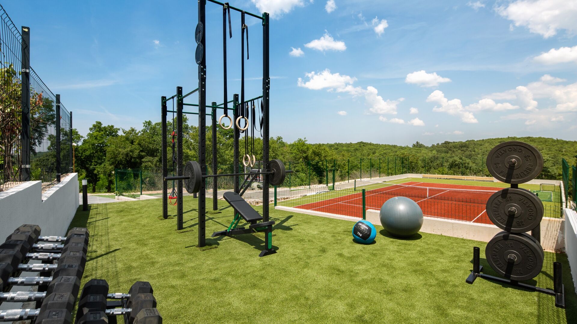 A gym with various exercise equipment, a tennis court, and a grassy area.