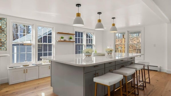 Una cocina moderna con una isla grande, taburetes de bar, luces colgantes y ventanas amplias.