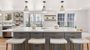 Una cocina moderna con una isla grande, taburetes de bar, lámparas colgantes y vistas al exterior.