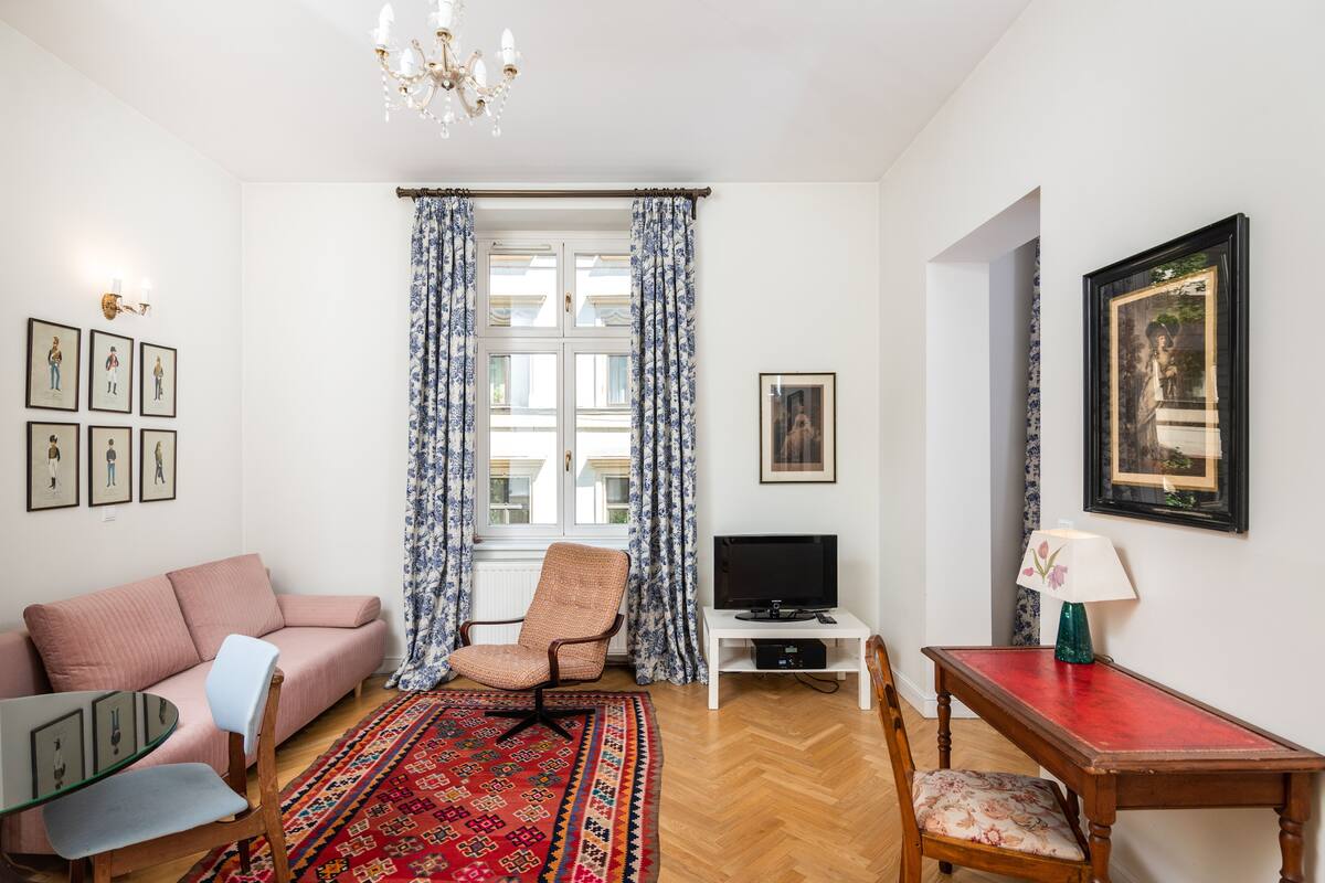 Een woonkamer met een bank, fauteuil, televisie en een bijzettafeltje met een lamp.