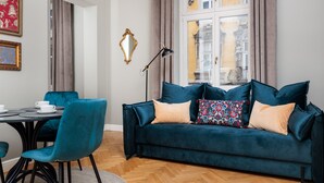Een moderne woonkamer met een blauwgroene bank, een eettafel met stoelen en een groot raam met gordijnen.