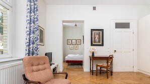 Een kamer met een gestreept fauteuil, een houten tafel met een stoel, een bed met een rode matras, en een witte deur.