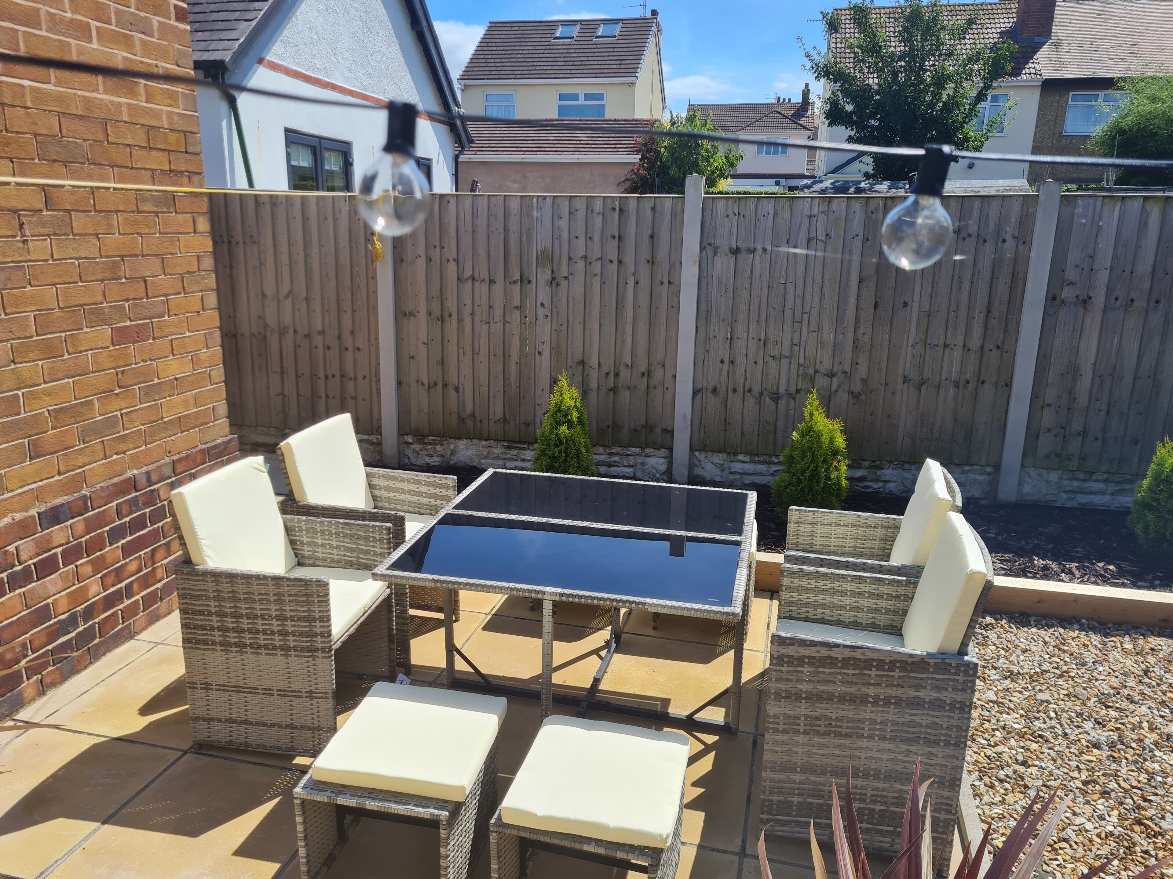 A patio with wicker furniture, a glass-top table, and a wooden fence in the background.