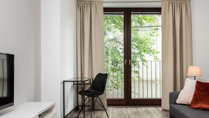Ett modernt vardagsrum med en tv, ett litet bord, en svart stol, en grå soffa och en balkong med gardiner.