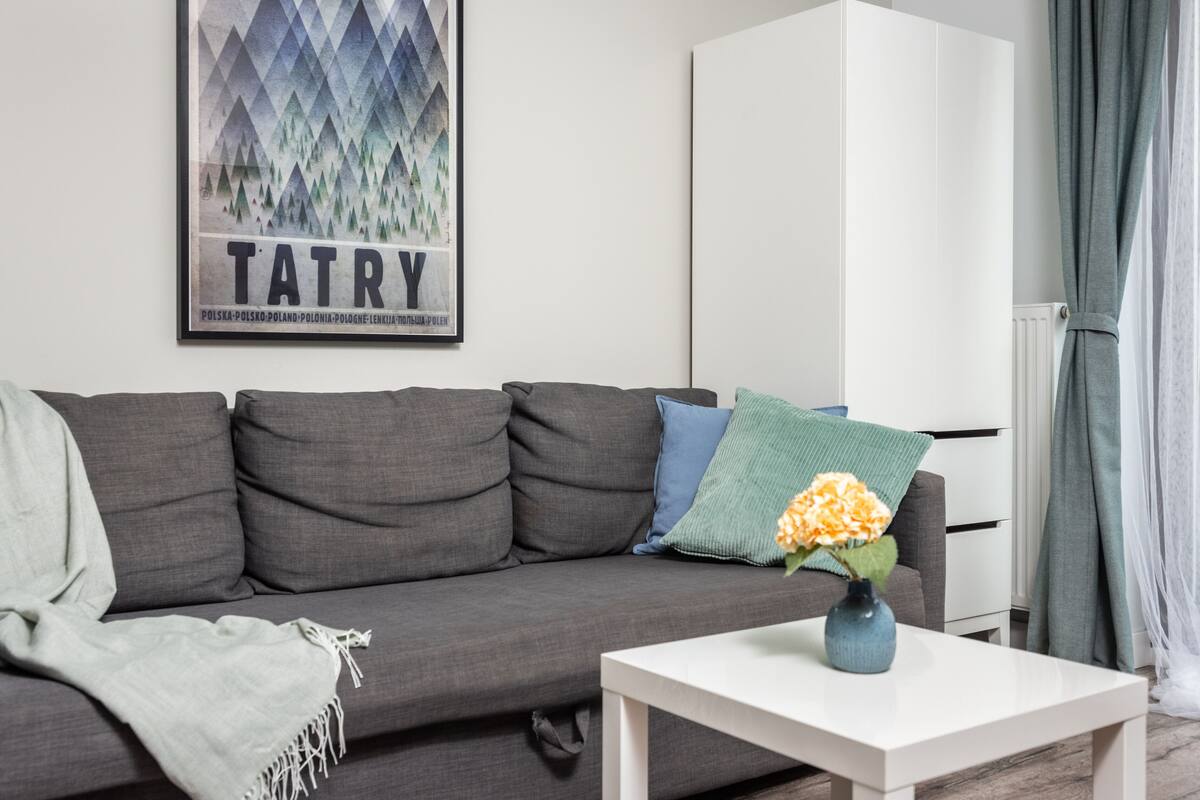 A modern living room with a grey sofa, a white table, and a framed poster on the wall.