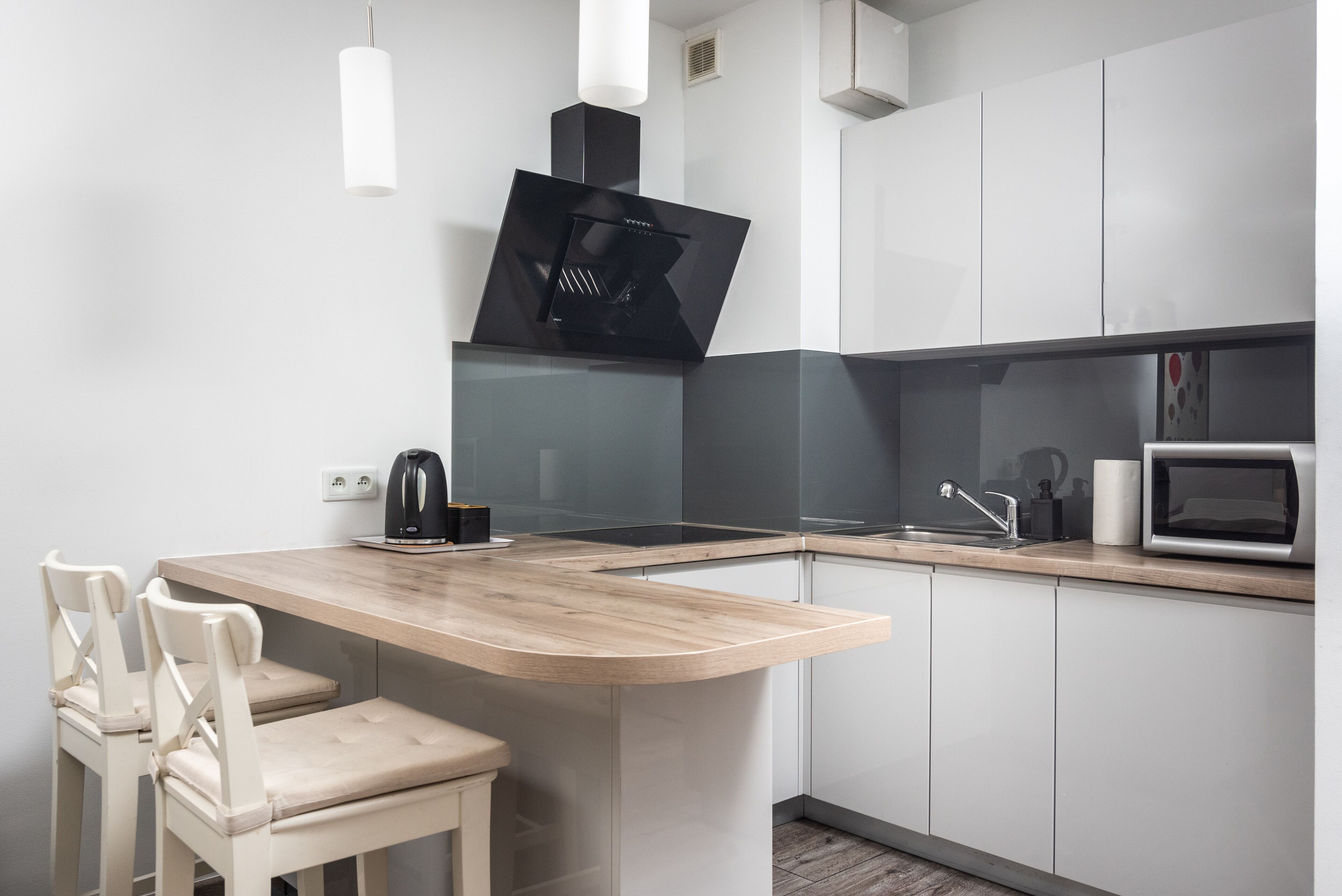 A modern kitchen with a curved island, white cabinetry, a black range hood, and a microwave.