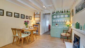 A cozy dining area with wooden chairs and a table, a bookshelf, and a wall with framed pictures.