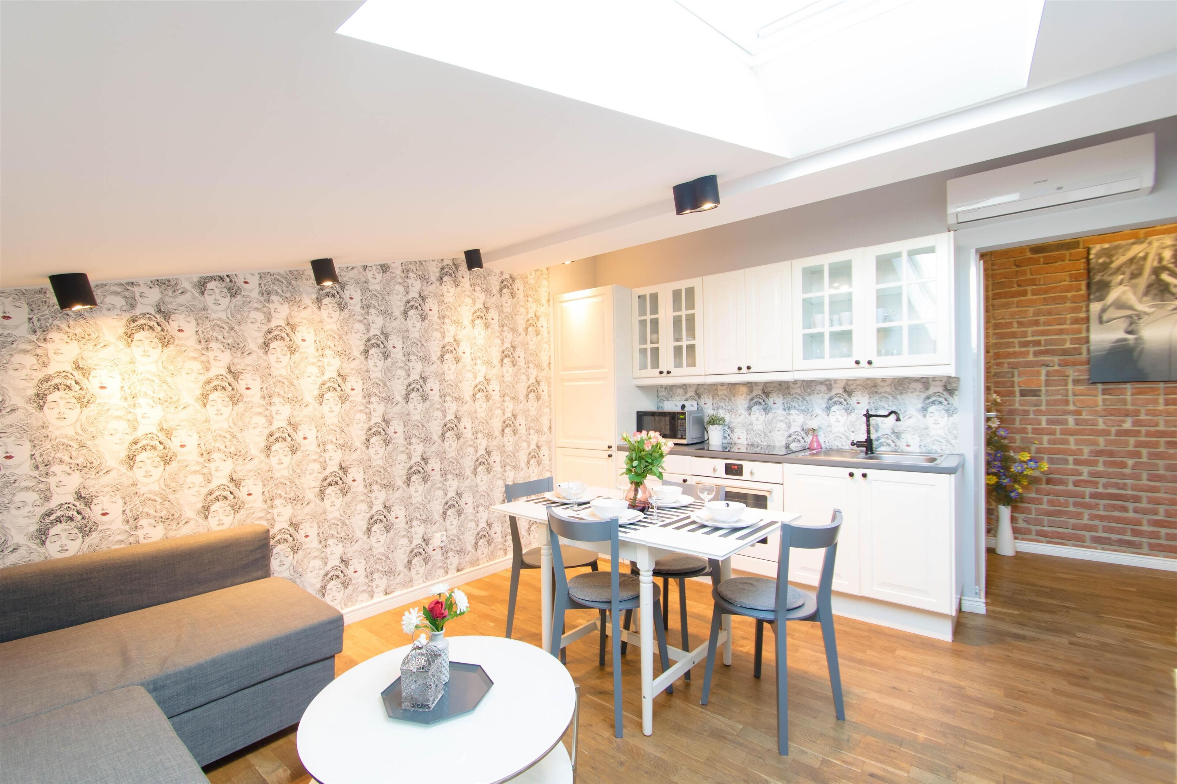 A modern kitchen with white cabinets, a dining area with a table and chairs, and a grey sofa.