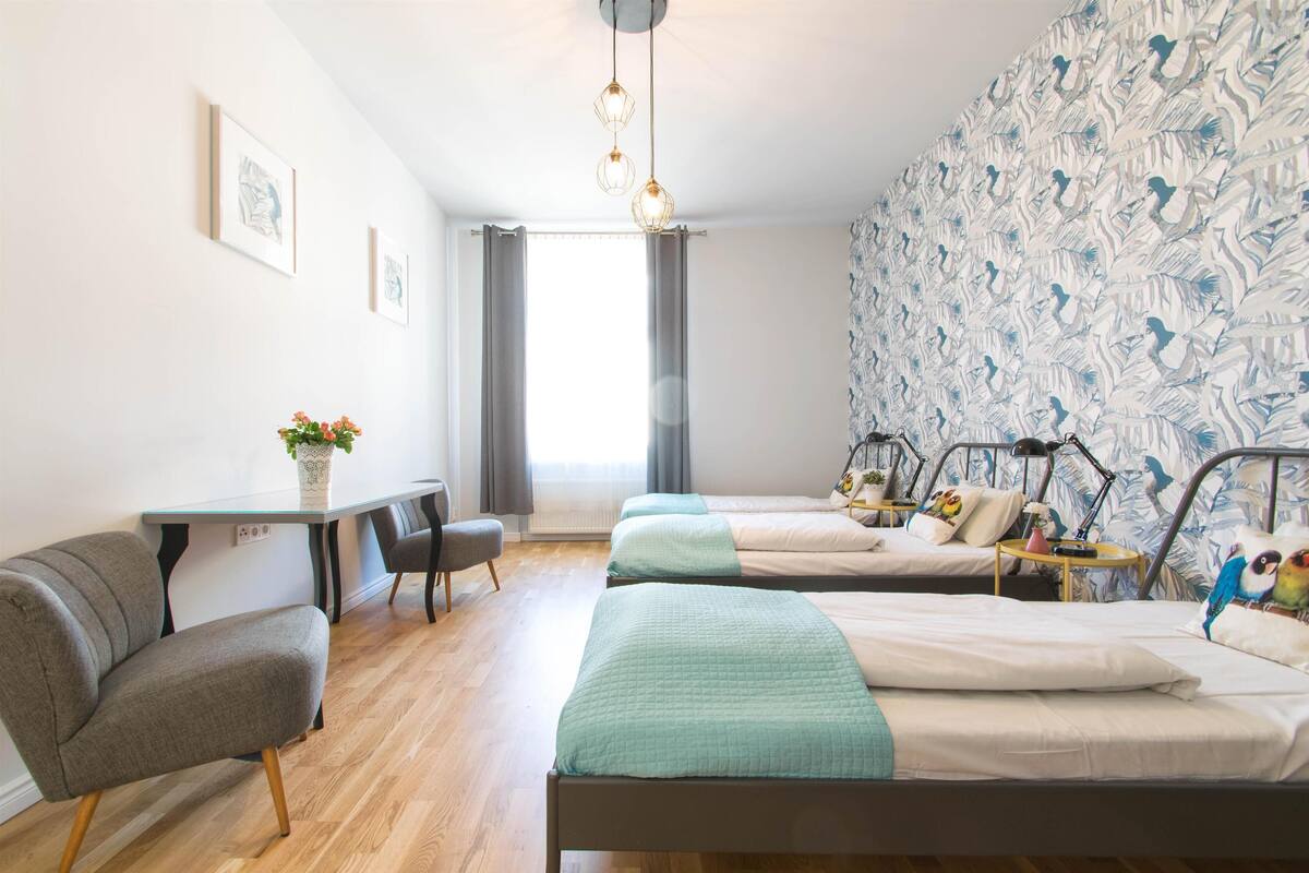 Une chambre avec deux lits simples, un bureau avec une chaise, une petite table avec un vase et un mur décoré de motifs.