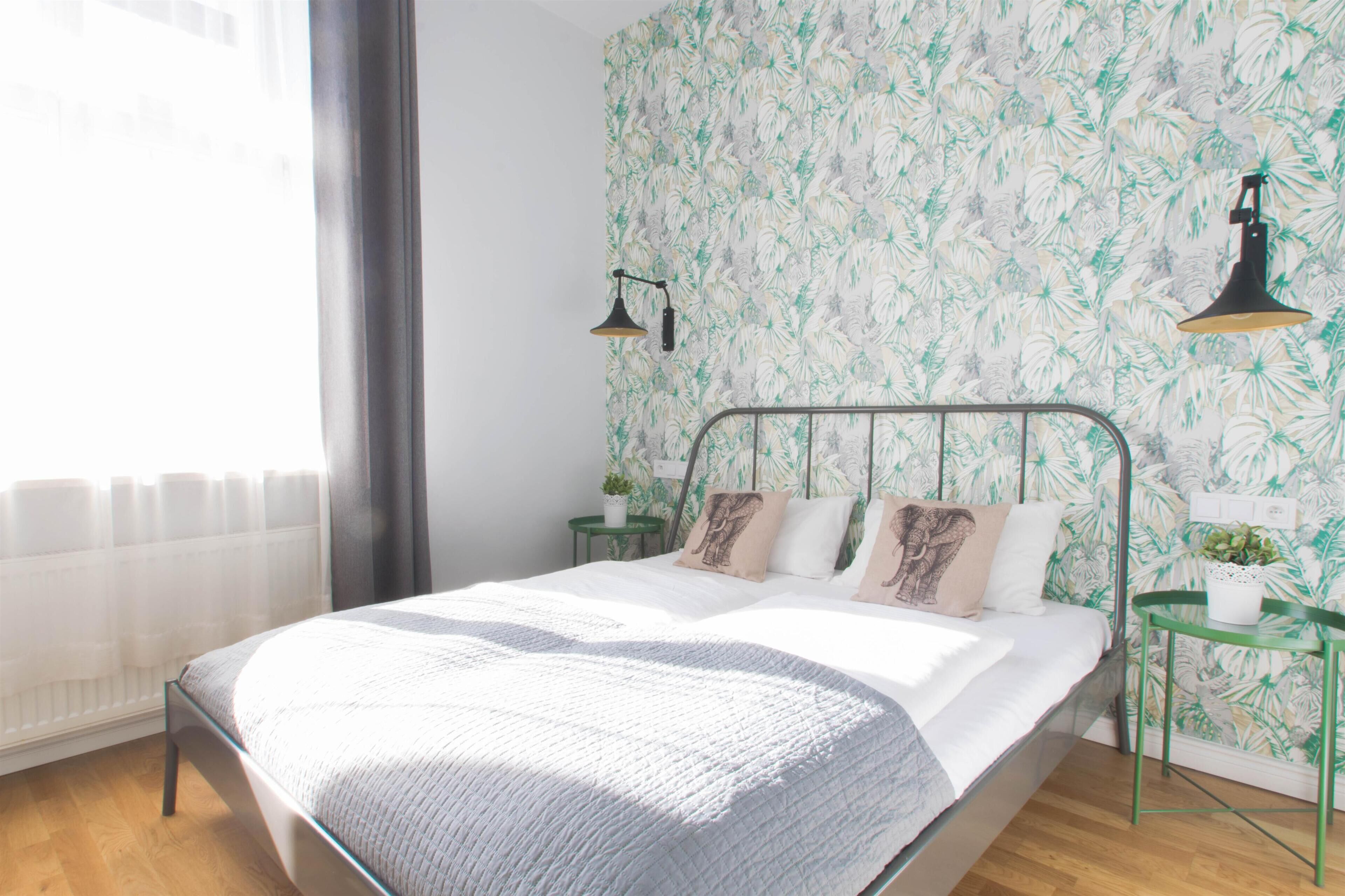 A modern bedroom with a metal bed frame, a large window with sheer curtains, and a floral wallpaper.