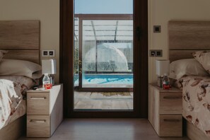 Un dormitorio con dos camas, cabeceros de madera, mesitas de noche con lámparas y vistas a una piscina a través de una puerta de cristal.