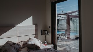 Een moderne slaapkamer met een groot bed, een nachtkastje met een lamp en uitzicht op een buitenzwembad door een glazen deur.