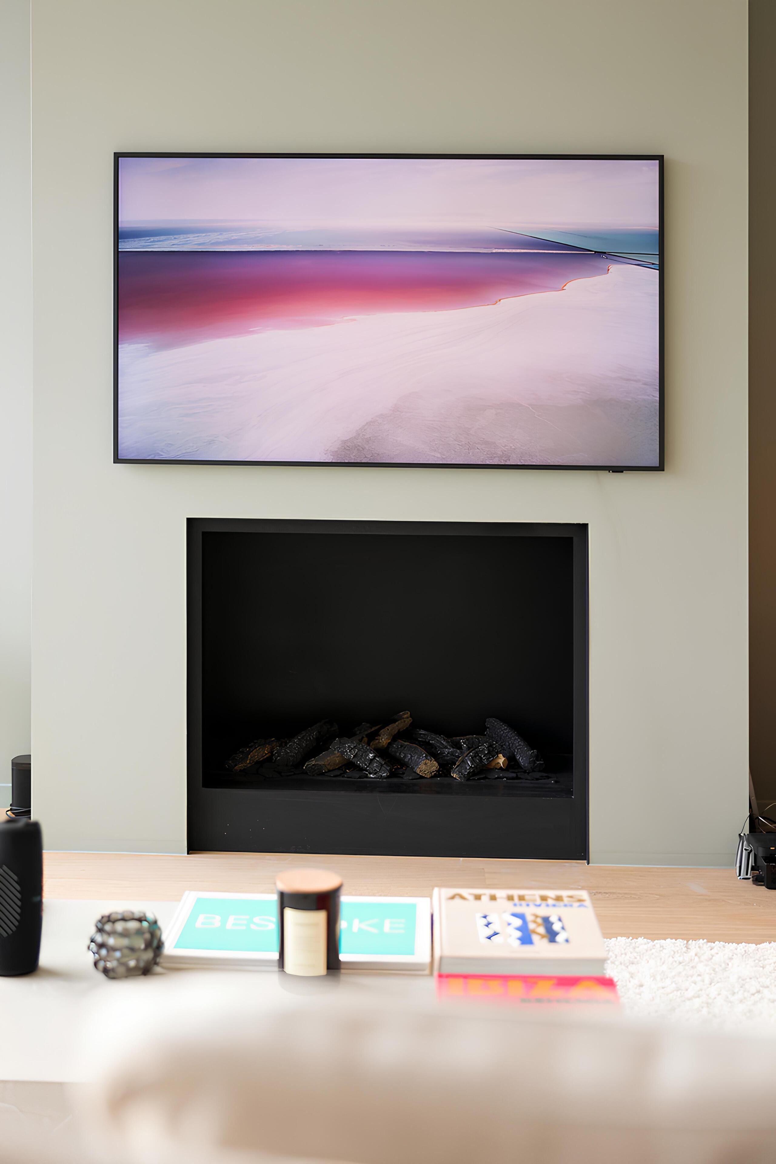 A living room with a large flat-screen TV mounted above a fireplace, a small table with books and a decorative item, and a white rug.