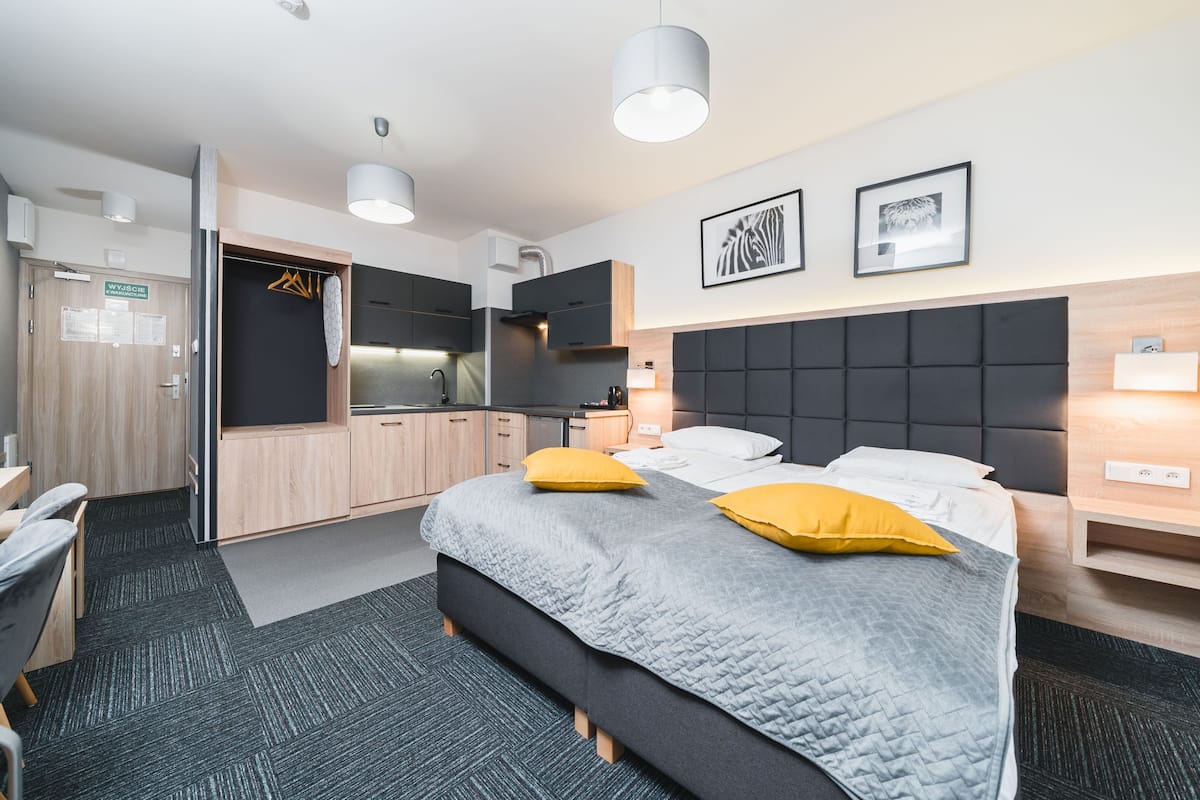 Quarto de hotel com cama, mesas de cabeceira, escrivaninha, cozinha compacta e banheiro.