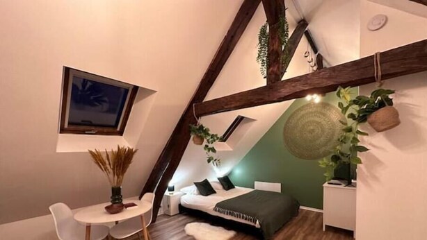 A cozy, triangular room with a bed, a small table, and chairs. - Le Nid Douillet - Studio (Beauvais)