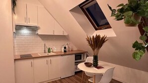 A compact kitchen with white cabinets, a wooden countertop, a built-in oven, and a small dining table with chairs. - Le Nid Douillet - Studio (Beauvais)