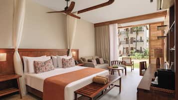 Habitación de hotel con una cama grande, un banco de madera, un escritorio y un balcón con vistas del edificio.