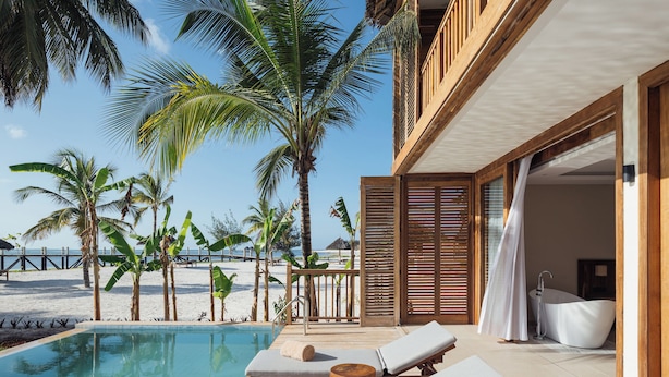 Un espace piscine avec des chaises longues, une terrasse en bois et une vue sur la plage et l’océan.