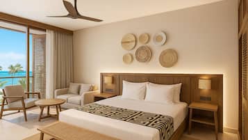 A modern hotel room with a large bed, two bedside tables, a sofa, a chair, and a view of the ocean.