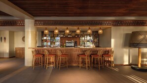 Un espace bar avec des tabourets de bar en bois, un comptoir où sont exposées des bouteilles et des lampes suspendues.