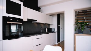 A modern kitchen with white cabinets, black appliances, and a wooden dining table. - RentPlanet - Świętego Mikołaja (Wroclaw)