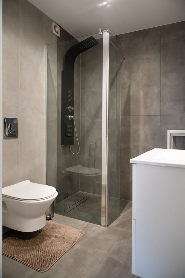 A modern bathroom with a glass-enclosed shower, a toilet, and a sink.