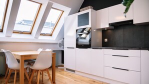 A modern kitchen with white cabinetry, a built-in oven, and a dining area with a wooden table and white chairs. - RentPlanet - Świętego Mikołaja (Wroclaw)