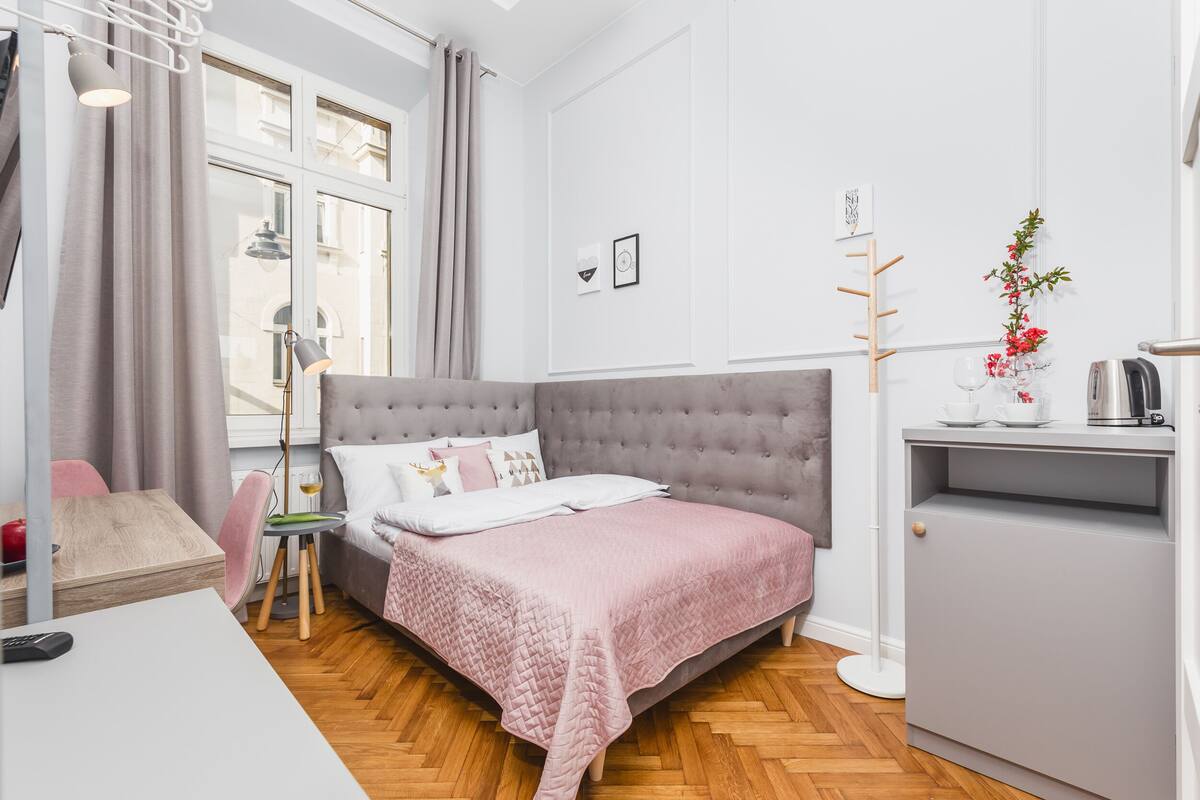 A modern bedroom with a tufted headboard, a bedside table with a lamp, a small desk, and a cabinet.