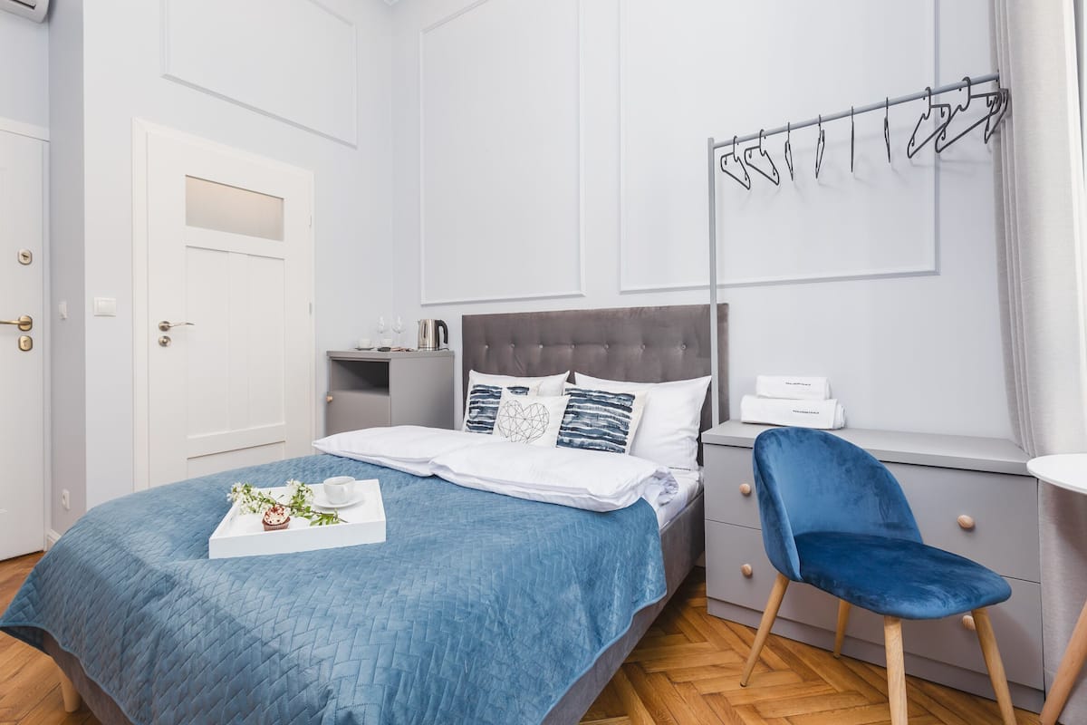 A neatly arranged bedroom with a bed, bedside table, chair, and a wall-mounted drying rack.