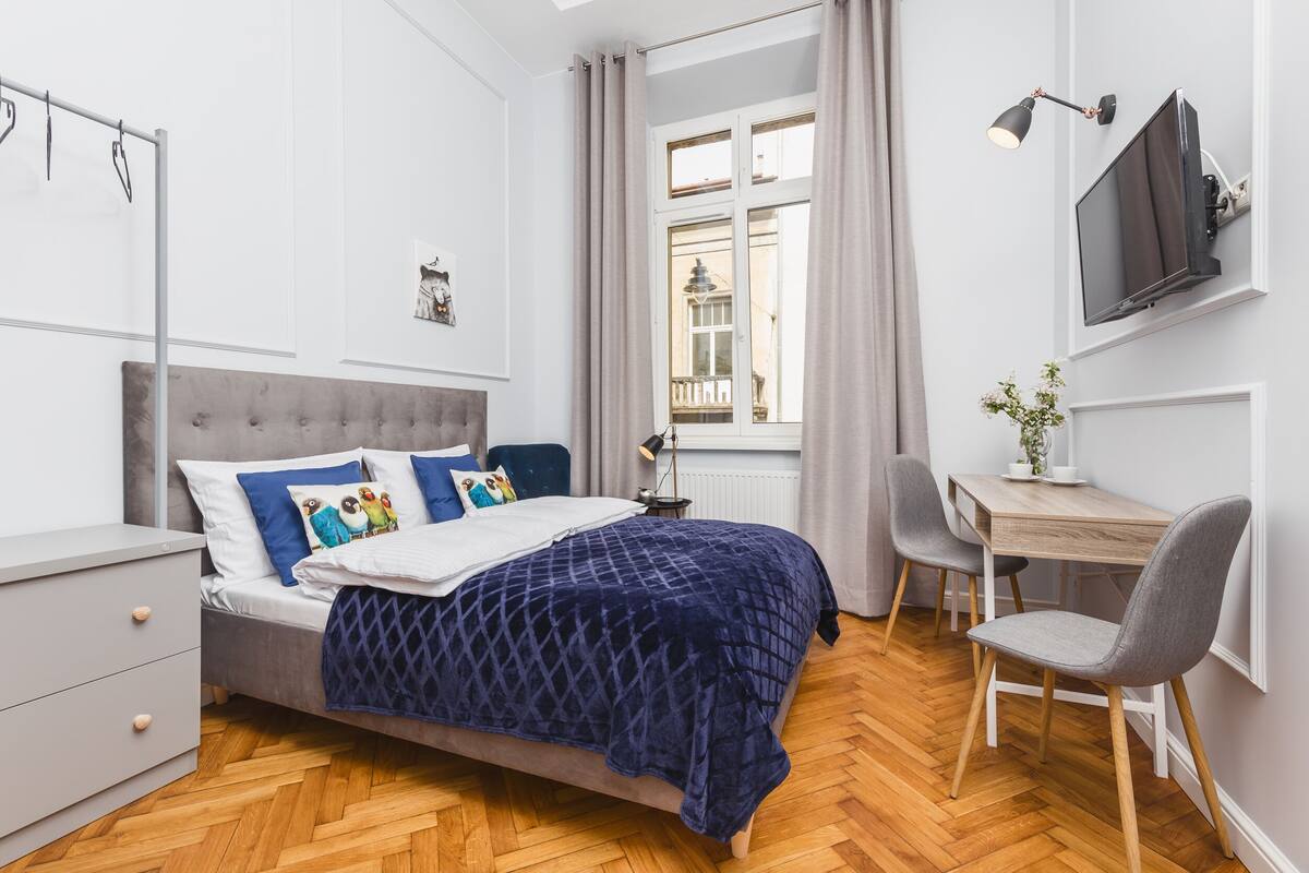 A modern bedroom with a bed, bedside table, desk, chair, and a TV mounted on the wall.