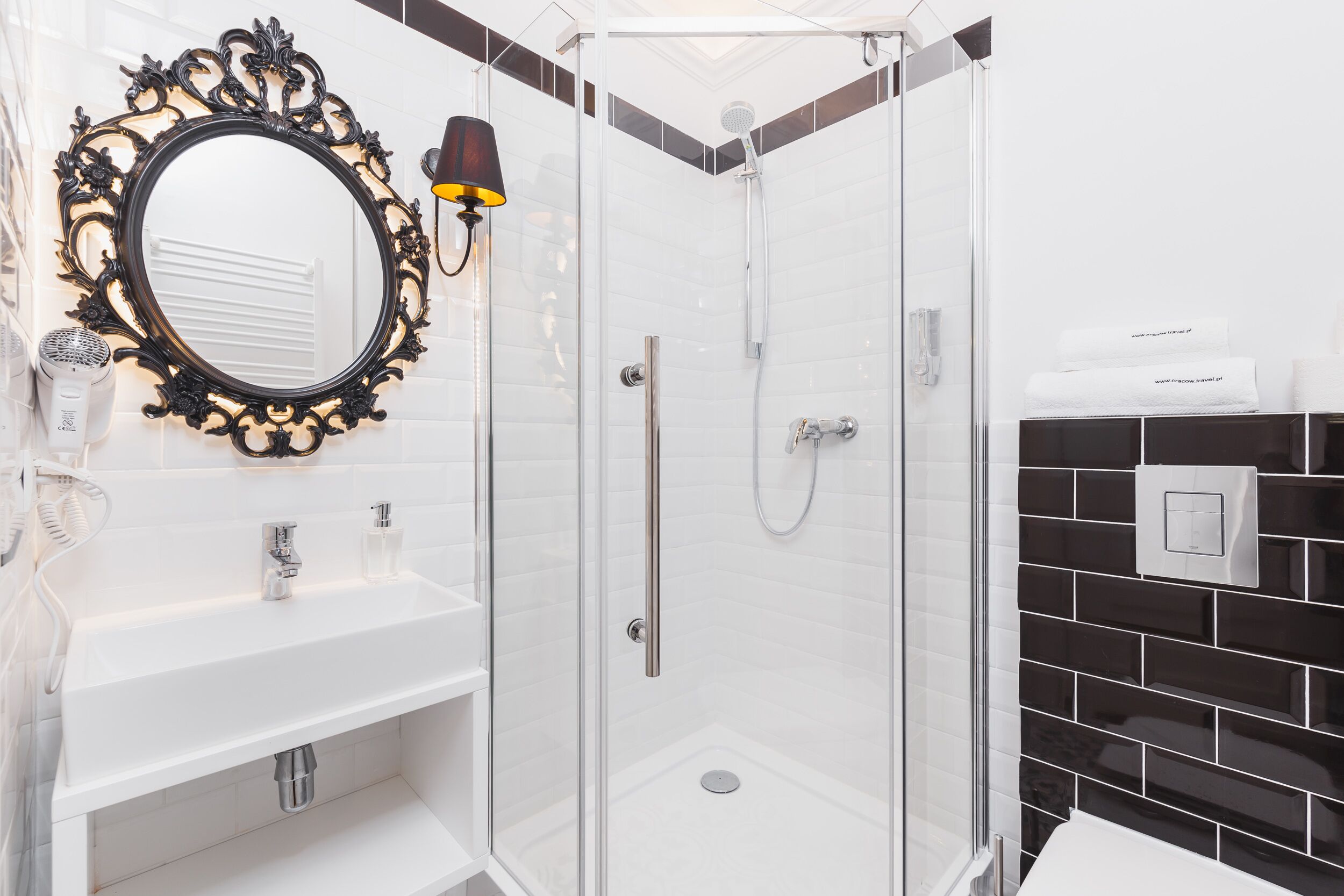 Une salle de bain moderne avec une douche à parois de verre, un lavabo blanc avec un miroir et des murs recouverts de carreaux noirs.